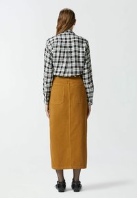 Chemise à carreaux noire, blanche et bordeaux, associée à une jupe midi de couleur moutarde avec deux poches arrière et une coupe droite.