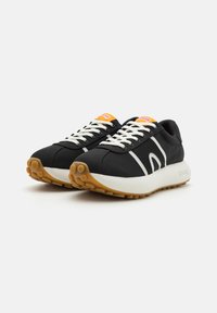 Schwarze Sportschuhe mit weißen Schnürsenkeln, die ein weißes Streifenmuster und eine Sohle aus Gummi haben. Bemerkensaktes orangenes Akzent auf der Zunge.