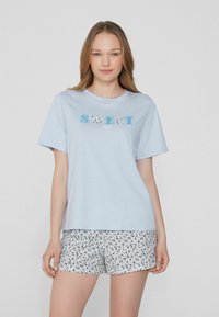 Světle modré bavlněné tričko s nápisem "SWEET night", v kombinaci s bílými šortkami s modrým květinovým vzorem. Krátké rukávy a volný střih.