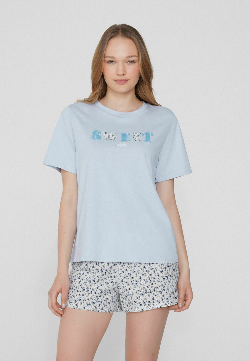 Světle modré bavlněné tričko s nápisem "SWEET night", v kombinaci s bílými šortkami s modrým květinovým vzorem. Krátké rukávy a volný střih.