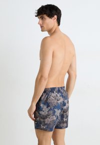 Pantaloni de baie pentru bărbați, cu un model floral albastru, talie elastică și buzunare laterale. Materialul pare neted, cu un design ușor.