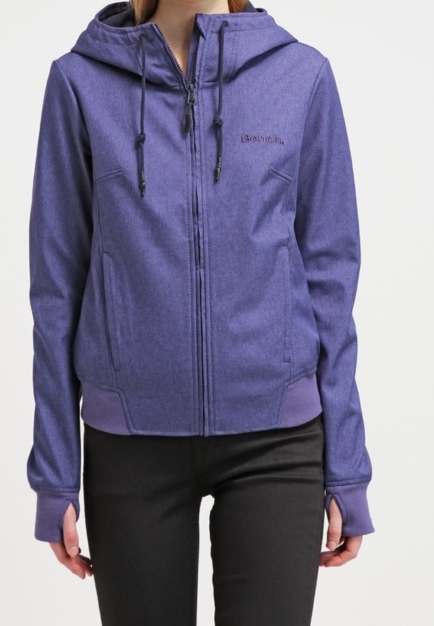 Femme portant un sweat à capuche violet à fermeture éclair avec cordons, poches latérales et manches avec trous pour le pouce, associée à un pantalon noir.