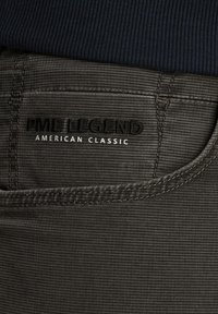 Donkergrijze textuur jeans met een ribbelachtige uitstraling. Heeft zwarte borduursels met de teksten "PME LEGEND" en "AMERICAN CLASSIC."