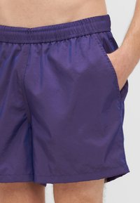 Pantaloni da bagno leggeri viola con vita elastica, tasche laterali e texture liscia e lucida. Design semplice, senza motivi né dettagli.