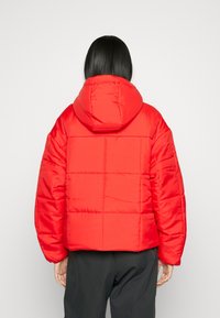 Röd puffjacka med huva, med en vadderad design och en glänsande yta. Korta längd med vida ärmar och en avslappnad passform.