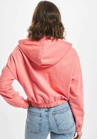Crop hoodie i korallrosa bomull, med stor hette, lange ermer og elastisk hem. Kombinert med lyseblå høytlivsjeans.