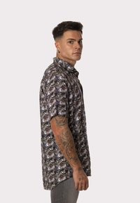 Camisa de botones de manga corta con un patrón de calaveras en blanco y negro sobre un fondo oscuro. Presenta un cuello abierto y un corte relajado.