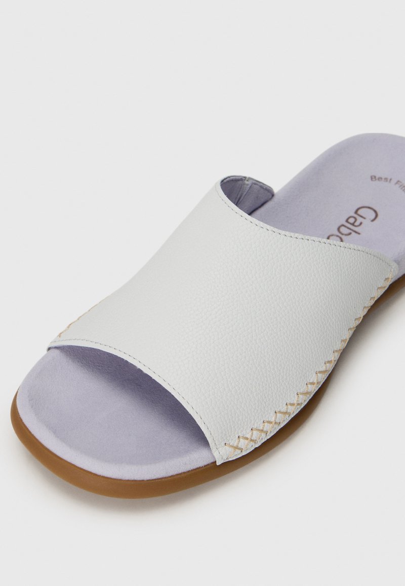 Weißes Leder-Slide-Sandalen mit lila Innensohle, breitem Riemen und gesteppten Akzenten an der Seite, flacher Sohle und glatter Textur.