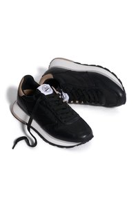Scarpe sportive nere con tomaia in pelle texturizzata, dettagli in beige e suola piatta bianca. Presentano lacci rotondi e un logo sulla linguetta.