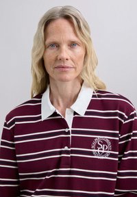 Weinrot gestreiftes Poloshirt mit weißem Kragen und Knopfleiste. Verfügt über marineblaue und cremefarbige Streifen, Logo auf der linken Brust. Aus weichem Baumwollstoff.