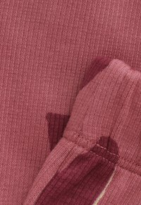 Close-up van gevouwen roze gebreide stof met zichtbare stiksels en een gestructureerd breipatroon.