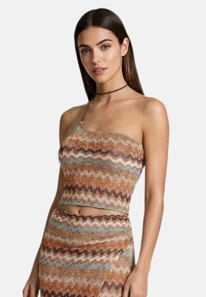 Donna che indossa un crop top lavorato a maglia multicolore a zigzag senza maniche e una gonna abbinata a vita alta, posando davanti a uno sfondo semplice.