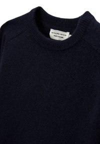 Pull en cachemire bleu marine avec un col rond côtelé et des manches raglan. Présente une texture douce et une étiquette indiquant "MONOPRIX PREMIUM PUR CACHEMIRE."