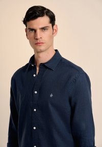 Camisa abotonada de manga larga en azul marino, hecha de un tejido texturizado, con un sutil logotipo bordado y botones blancos a lo largo del frente.