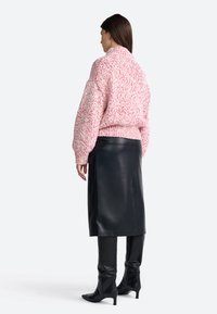 Pulover greu roz și alb, tricotat, cu mâneci tip balon, asortat cu o fustă elegantă din piele neagră și cizme negre cu vârf ascuțit până la genunchi.
