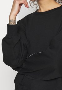 Sweatshirt noir avec encolure ronde, manches bouffantes et texte brodé contrastant à l'avant. Tissu doux et texturé.