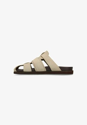 Sandalo da uomo beige in pelle scamosciata con tre ampie fasce, design con punta aperta e suola piatta marrone scuro con battistrada testurizzato.