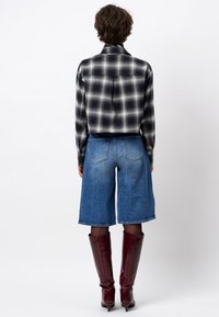 Zwart-wit geblokte cropped shirt, blauwe denim Bermuda shorts en glanzende bordeauxrode knielange laarzen met een spitse neus.