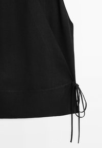 Zwarte mouwloze stoffen top met een koorddetail bij de zoom op een witte achtergrond.