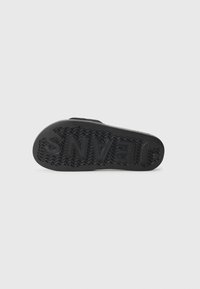 Semelle en caoutchouc noir avec motif de grip texturé et logo "VANS". Présente une forme arrondie avec un profil plat et des bords renforcés.