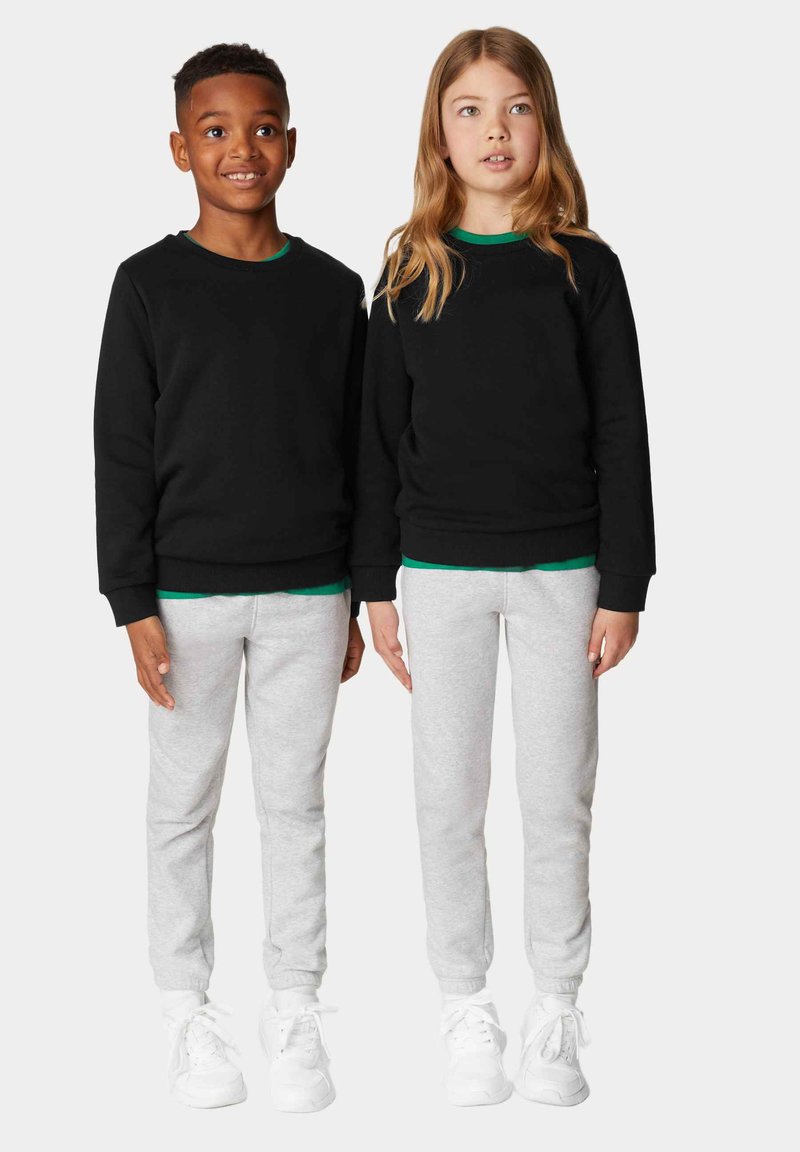 Due bambini stanno fianco a fianco, indossando felpe nere sopra magliette verde girocollo. Combinano questi con pantaloni leggeri grigi e sneakers bianche.