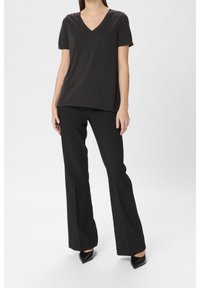 Svart t-shirt med V-krage gjord av mjukt tyg, ihopparad med skräddarsydda svarta utsvängda byxor. Outfiten har en slät textur och en figurnära silhuett.