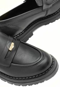 Czarne skórzane mokasyny z okrągłym noskiem, z detalami w postaci przeszyć oraz małym metalowym akcentem z logo. Gruba, gumowa podeszwa o dobrej przyczepności.