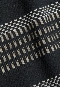 Tissu tricoté noir avec des rangées de petits motifs géométriques abstraits beiges et blancs formant un motif horizontal symétrique.