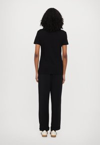 Black t-shirt with short sleeves, paired with black, loose-fit trousers and light-colored shoes; smooth texture and simple design.