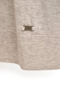 Suéter de punto beige con dobladillo acanalado. Presenta una pequeña etiqueta metálica que dice "POLO CLUB" cerca de la parte inferior, destacando la textura y el diseño.