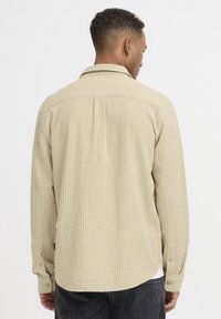 Beige langærmet skjorte med lodrette striber, knappet krave og manchetter. Blødt stof med en afslappet pasform og rundet bund.