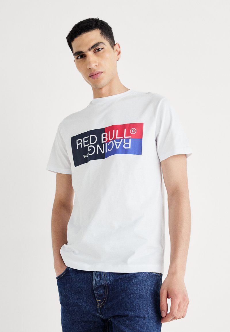 Balts kokvilnas T-krekls ar uzboldītu, daudzkrāsainu "RED BULL RACING" grafiku, īsām piedurknēm un apaļu kakla izgriezumu. Saskaņots ar tumšu džinsu.