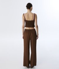 Top corto marrone arricciato con spalline sottili, abbinato a pantaloni larghi marroni a gamba larga con vita elastica e tasche posteriori.
