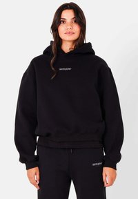 Zwarte hoodie gemaakt van zacht materiaal met een relaxed fit, voorzien van een klein logo op de borst en geribbelde manchetten en onderrand.