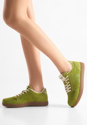 Des baskets en daim vert avec une semelle marron clair, des lacets beiges et des accents texturés. Le design comprend des perforations pour la ventilation.