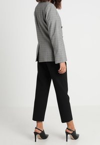 Blazer à carreaux gris avec une coupe ajustée, deux boutons et un détail fente, associé à un pantalon court noir et des chaussures à talons hauts.