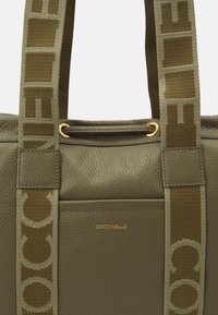 Olijfgroene leren tote met een gecreëerde oppervlakte, gouden hardware accenten en logo aan de voorkant. Heeft contrasterende geweven handvatten.