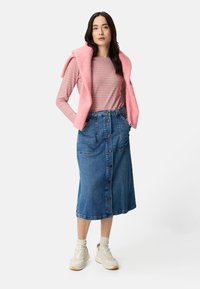 Hellrosa Pullover locker über den Schultern getragen, gestreiftes Langarmshirt, Jeans-Midirock mit vorderen Knöpfen und Taschen, beigen Sneakers.