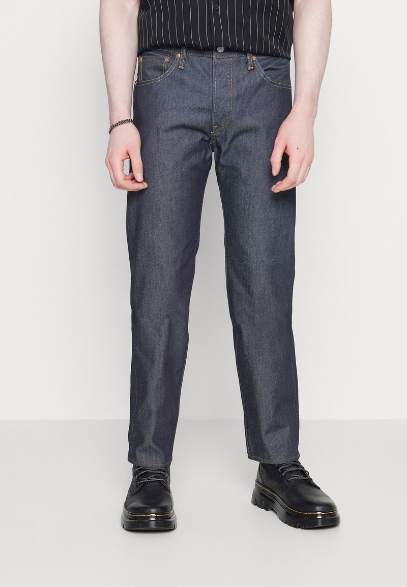 Mörkblå denimjeans med rak skärning, femficksdesign och orangea sömnadsdetaljer. Kombination med svarta snörboots.