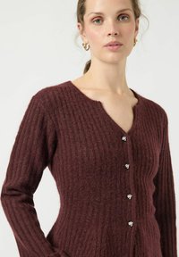 Cardigan bordeaux a costine realizzato in morbido materiale a maglia, con scollatura a V e bottoni color argento lungo la parte anteriore. Maniche lunghe incluse.