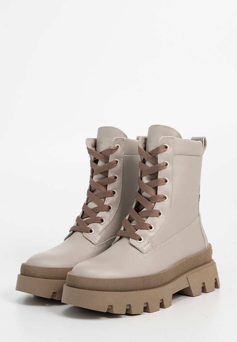 Beige Schnürkampfstiefel mit einer massiven braunen Sohle. Obermaterial aus glattem synthetischem Leder, runde Zehenform und verstärkte Ösen.