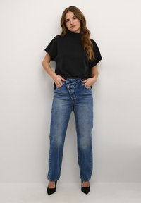 Schwarzes Kurzarmoberteil kombiniert mit hochtaillierten, mittelblauen Denim-Jeans. Das Outfit wird durch schwarze spitz zulaufende Absätze für einen eleganten Look ergänzt.