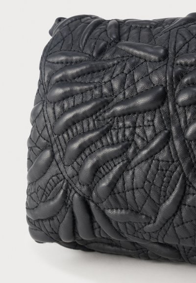 Κοντινή λήψη επιφάνειας από μαύρο δέρμα με ανασηκωμένα, μαξιλαρωμένα αφηρημένα σχήματα και λεπτομερή ραφή που σχηματίζουν μια υφή.