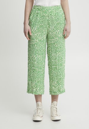 Pantalons cropped à motif vert avec un tissu texturé présentant un design géométrique, une taille élastique et des poches latérales, associés à des baskets blanches.