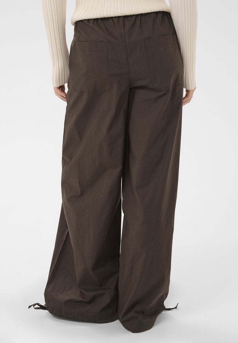 Personne portant un pantalon large sombre avec des poches à l’arrière et des cordons aux ourlets, assorti à un pull léger côtelé.