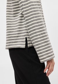 Top de manga longa às riscas cinza e branco com um corte descontraído, fendas laterais e textura suave, combinado com calças pretas.