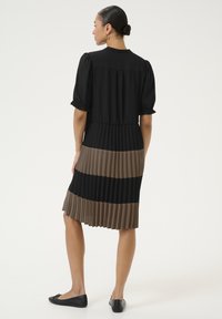 Schwarzes und braunes plissiertes Kleid mit puffärmeligen kurzen Ärmeln, Rundhalsausschnitt und fließender Silhouette mit horizontalen Farbblöcken.