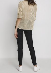 Beige struktureret bluse med lodrette linjer, korte ærmer, parret med tætsiddende sorte bukser og hvide plateau sneakers.