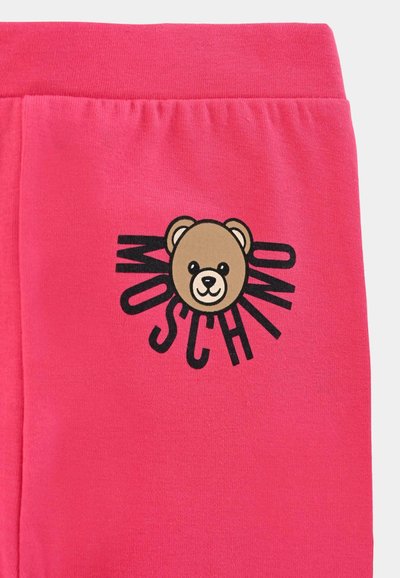 I joggers in cotone rosa presentano una grafica di un orso bruno con il testo "MOSCHINO" in nero, linee radianti attorno all'orso e una vita elastica.