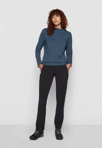 Blue patterned long-sleeve top with a hood, paired with black zippered pants and black footwear. Smooth texture and fitted design.